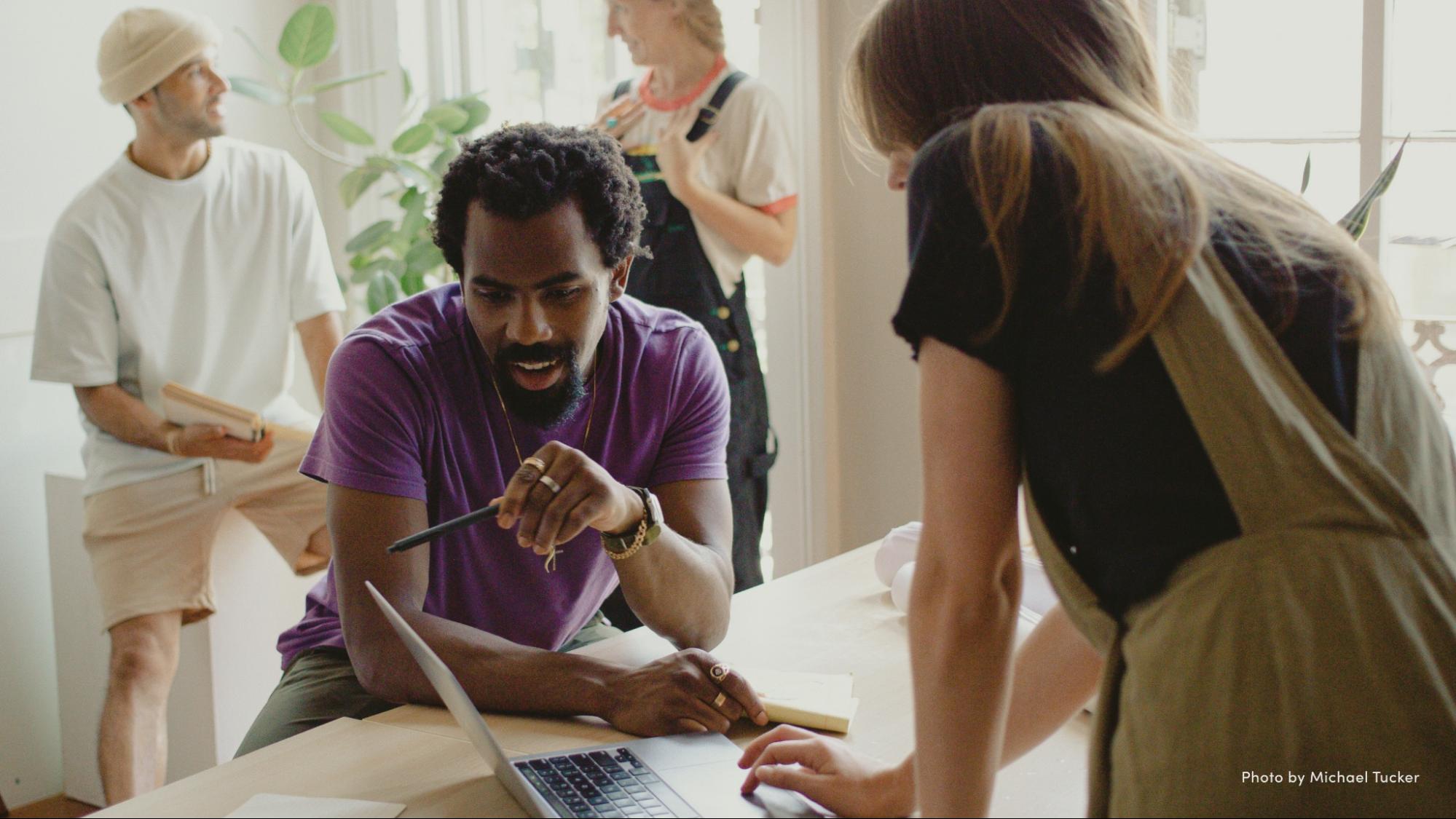 A group of people leaning over a table with a laptop.