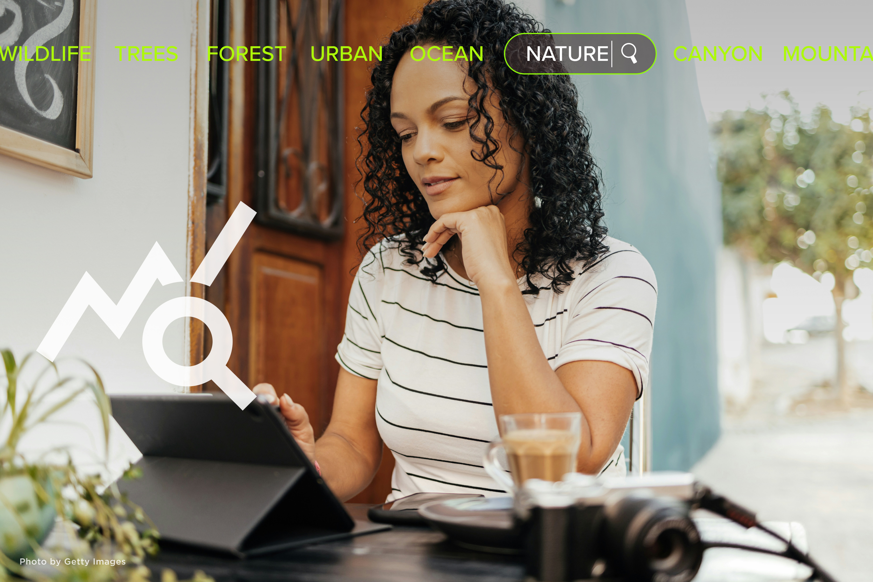 Woman sitting at an outdoor café, working on a tablet, with a camera sitting on the table nearby.